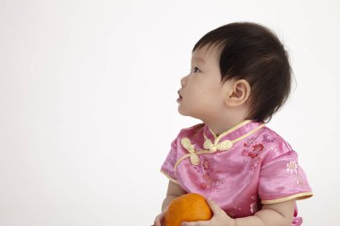 Çinli bebek tutan bir portakal cheomgsam giyiyor   