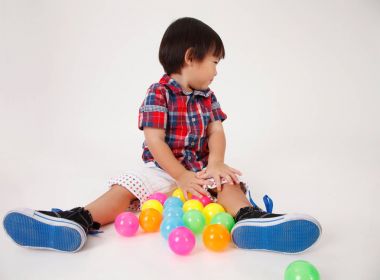 Çinli çocuk oynamak renkli topları önünde oturan