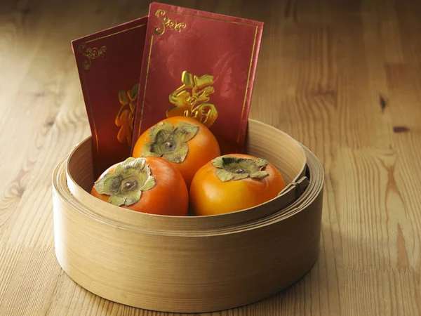 persimmons in a basket o with chinese red envelope-ang pao