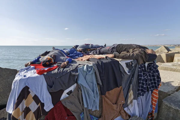 Italien, Medelhavet, Sicilien, Scoglitti (provinsen Ragusa); 8 mars 2011, afrikanska invandrare sover på ett betongblock i hamnen, medan kläderna torkar under solen - ledare — Stockfoto