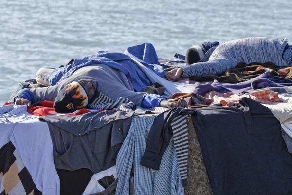 Italia, Mar Mediterraneo, Sicilia, Scoglitti (provincia di Ragusa); 8 marzo 2011, immigrati africani che dormono su un blocco di cemento nel porto, mentre i loro vestiti si asciugano sotto il sole - EDITORIALE — Foto Stock