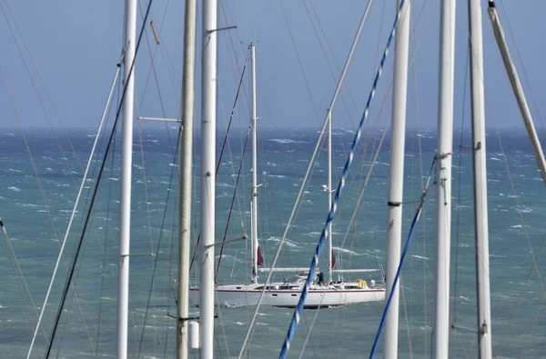 Itália, Sicília, Mar Mediterrâneo, Marina di Ragusa, mastros de barco à vela no porto e um barco à vela no mar — Fotografia de Stock