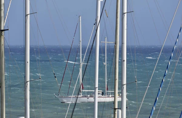 Itália, Sicília, Mar Mediterrâneo, Marina di Ragusa, mastros de barco à vela no porto e um barco à vela no mar — Fotografia de Stock