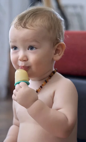 Портрет годовалого мальчика, облизывающего мороженое в помещении — стоковое фото