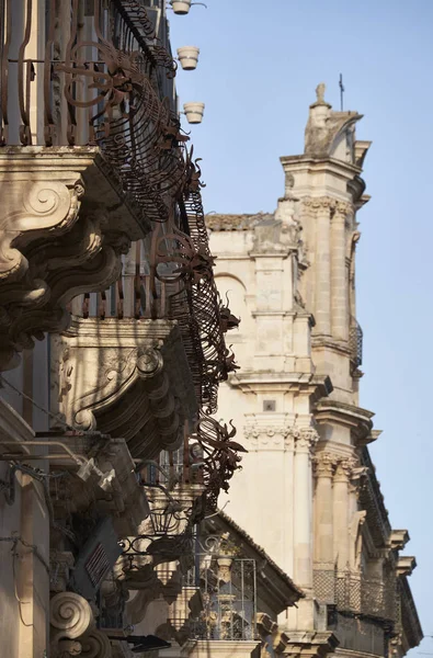 Italia, Sicilia, Scicli (provincia de Ragusa), antiguos balcones barrocos y la fachada de la iglesia de San Juan (siglo XVIII AC) en el fondo — Foto de Stock