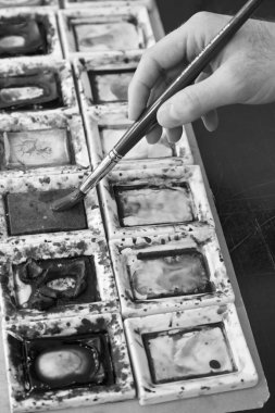 Boyacının eli boya fırçası ve renkleri tutuyor.