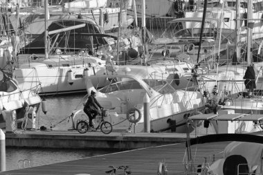 İtalya, Sicilya, Akdeniz, Marina di Ragusa (Ragusa Eyaleti); 10 Aralık 2019, limandaki bisiklet ve lüks yatlarda yaşayan kadın -