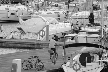 İtalya, Sicilya, Akdeniz, Marina di Ragusa (Ragusa Eyaleti); 28 Ocak 2020, limandaki bisiklet ve lüks yatlarda bir adam -