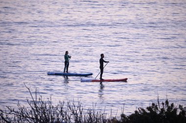 İtalya, Sicilya, Marina di Ragusa (Ragusa Eyaleti); 9 Şubat 2020, gün batımında kıyıda kürek çeken sörfçüler - Editör