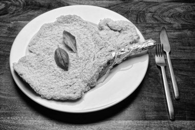 Yiyecek: Beyaz bir tabakta fesleğen yapraklı çiğ Milan pirzolası.