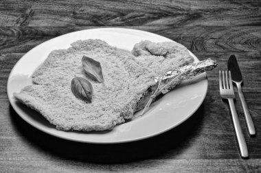 Yiyecek: Beyaz bir tabakta fesleğen yapraklı çiğ Milan pirzolası.