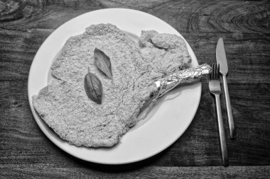 Yiyecek: Beyaz bir tabakta fesleğen yapraklı çiğ Milan pirzolası.