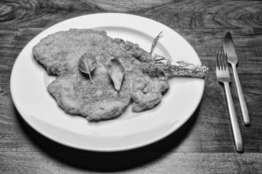 Yiyecek; kızarmış Milano pirzolası. Beyaz bir tabakta fesleğen yapraklı biftek.