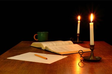 Mum ışığında aydınlatılmış kitap, kalem ve kağıt