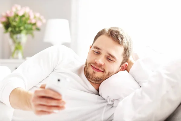 Man liggend in bed met smartphone — Stockfoto