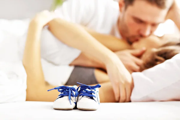 Casal beijando na cama e sapatos de bebê — Fotografia de Stock