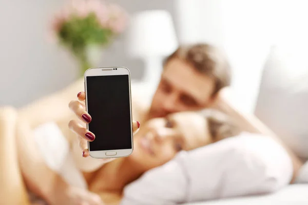 Jovem casal na cama com smartphone — Fotografia de Stock