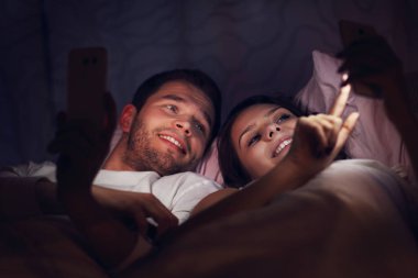 Genç çift yatakta akıllı telefonlar kullanarak 