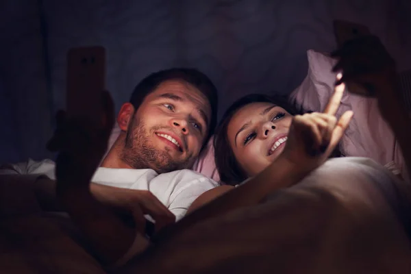 在床上使用智能手机的年轻夫妇 — 图库照片
