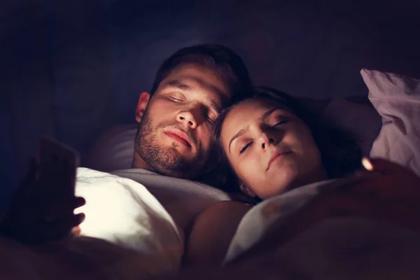 Casal jovem usando smartphones na cama — Fotografia de Stock