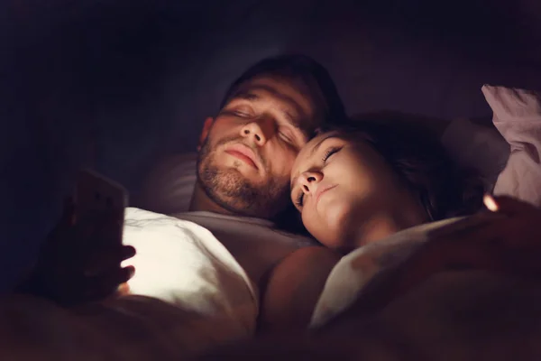 Młoda para w łóżku przy użyciu smartfonów — Zdjęcie stockowe