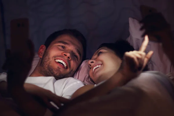 Junges Paar mit Smartphones im Bett — Stockfoto