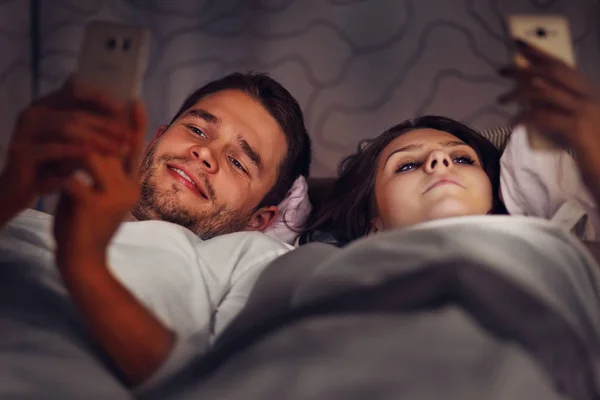 Junges Paar mit Smartphones im Bett — Stockfoto