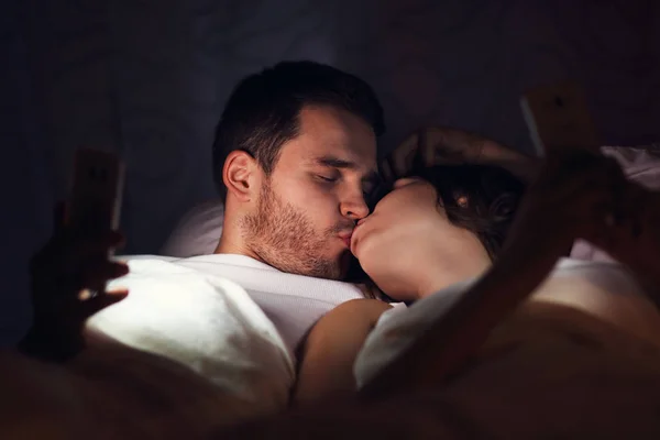 Casal jovem usando smartphones na cama — Fotografia de Stock