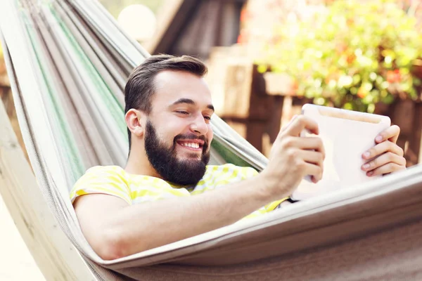Muž odpočívá v houpací síti s tabletem — Stock fotografie