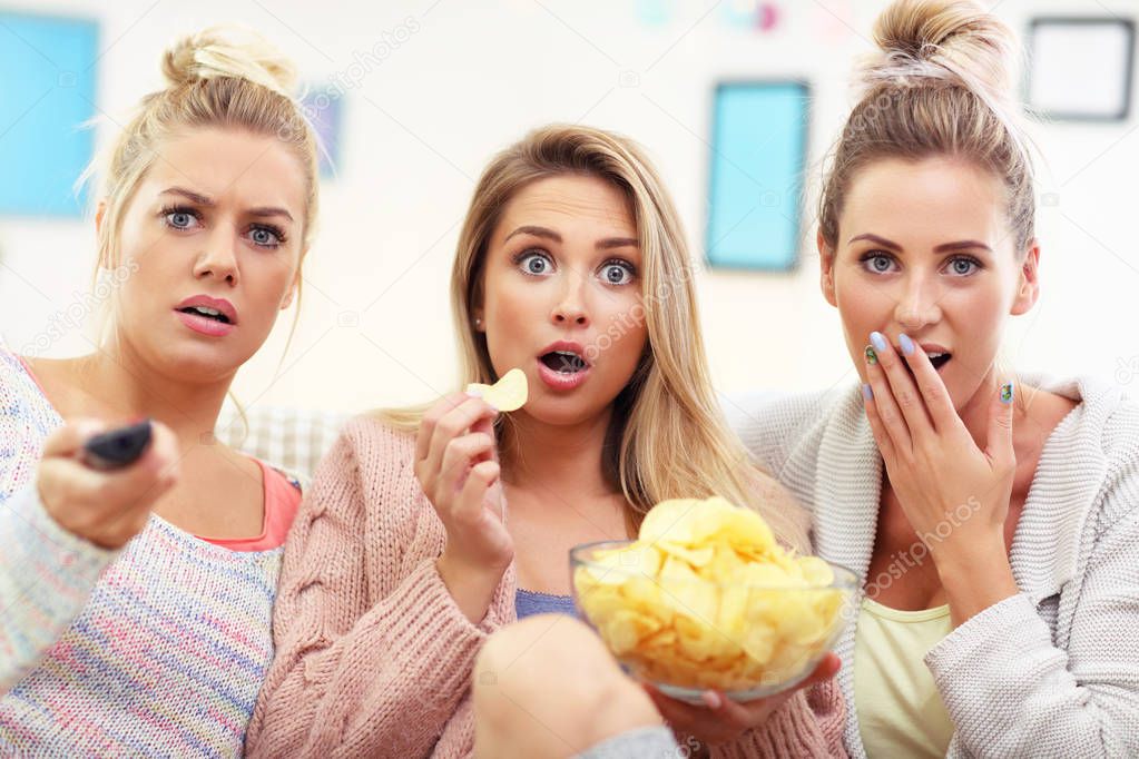 Three beautiful young women watching tv at home