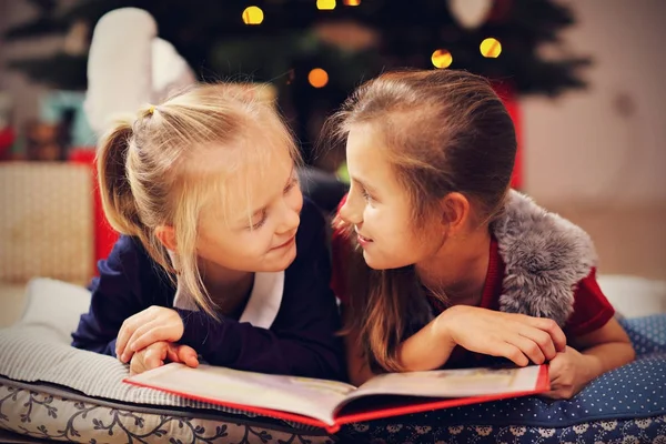 Two cute little sisters reading story book together under Christmas tree — Stock Photo, Image