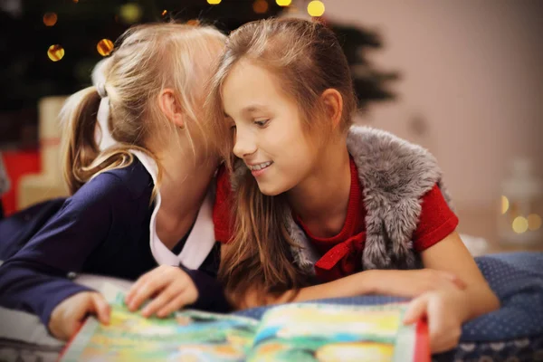 Two cute little sisters reading story book together under Christmas tree — Stock Photo, Image