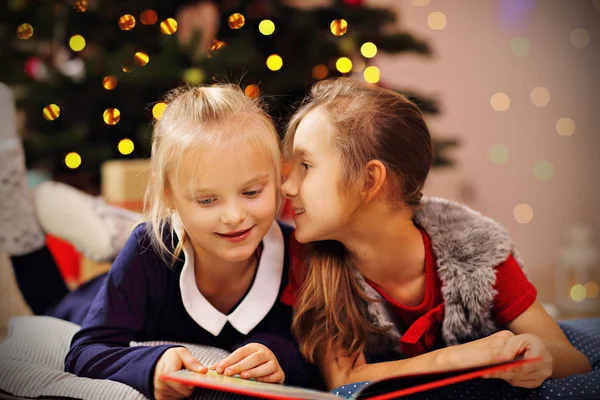 Duas irmãs pequenas bonitos lendo livro de história juntos sob a árvore de Natal — Fotografia de Stock
