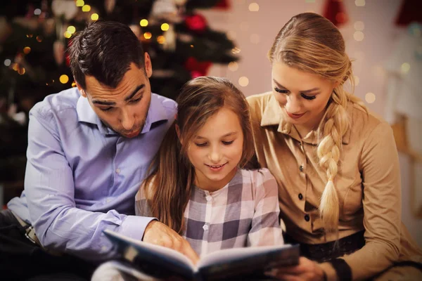 Family reading story book together under Christmas tree