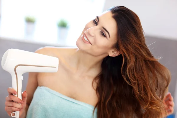 Young woman using hair dryer in bathroom in the morning — Stock Photo, Image