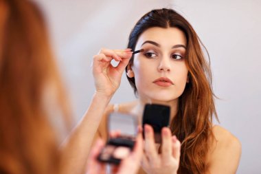 Çekici genç kadının banyo aynaya bakarak makyaj yapması