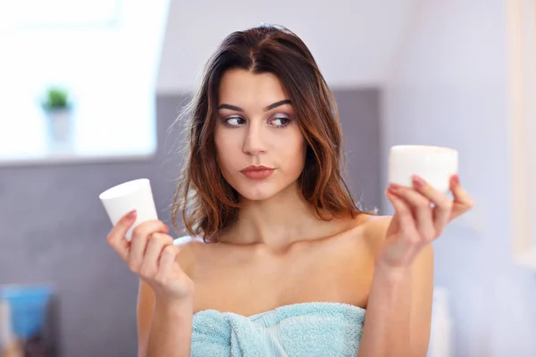 Jeune femme debout dans la salle de bain et l'application de crème visage le matin — Photo