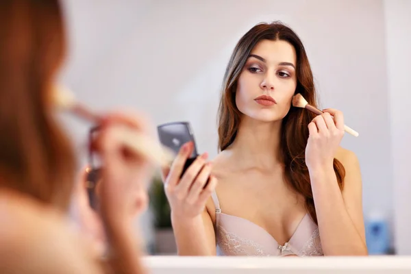 Jovem atraente fazendo maquiagem enquanto olha para o espelho no banheiro — Fotografia de Stock