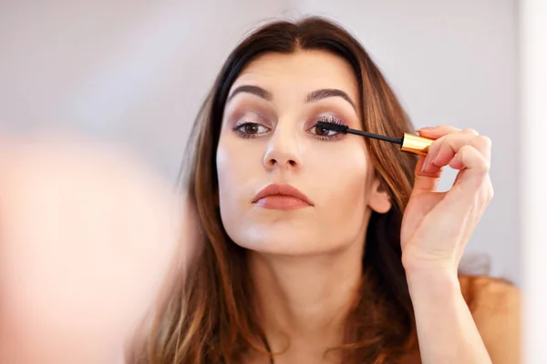 Aantrekkelijke jonge vrouw make-up doen tijdens het kijken naar de spiegel in de badkamer — Stockfoto