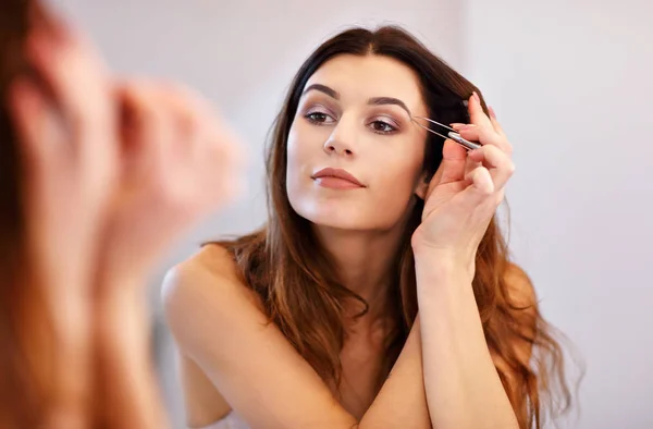 Attraente giovane donna che fa il make-up guardando lo specchio in bagno — Foto Stock