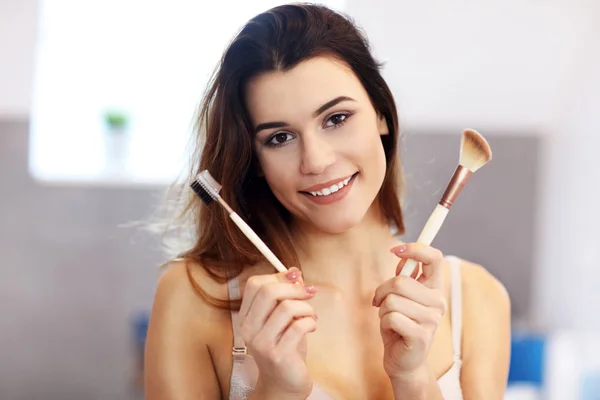 Atractiva joven mujer haciendo maquillaje mientras mira el espejo en el baño —  Fotos de Stock