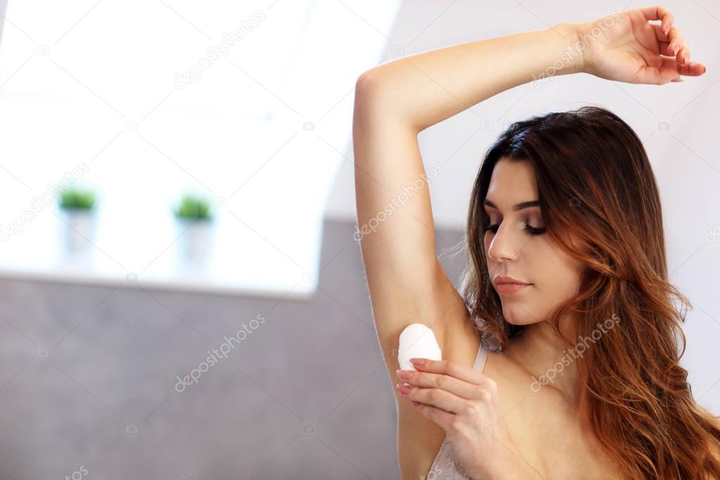 Woman applying deodorant on armpit in bathroom