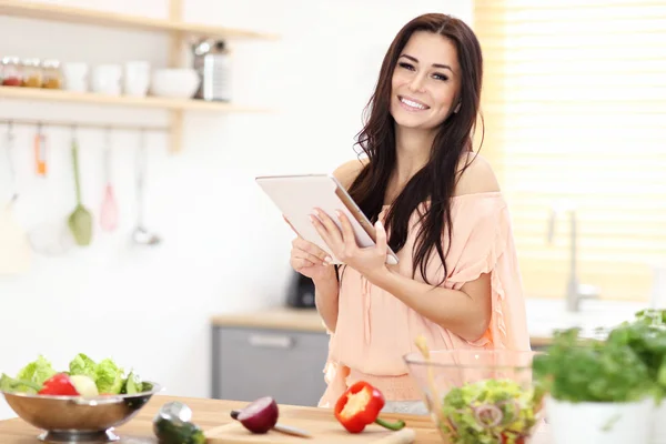 Mulher feliz preparando salada na cozinha moderna e segurando tablet — Fotografia de Stock