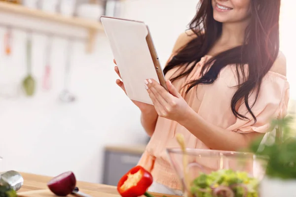 Glückliche Frau bereitet Salat in moderner Küche zu und hält Tablette in der Hand — Stockfoto