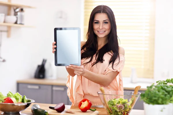 Glückliche Frau bereitet Salat in moderner Küche zu und hält Tablette in der Hand — Stockfoto