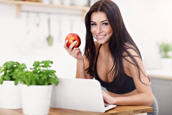 Ταιριάζει χαμογελώντας νεαρή γυναίκα με το μήλο σε σύγχρονη κουζίνα — Φωτογραφία Αρχείου