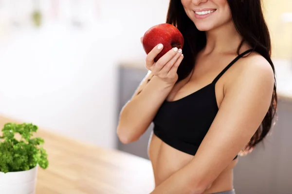 Fit jeune femme souriante avec pomme dans la cuisine moderne — Photo