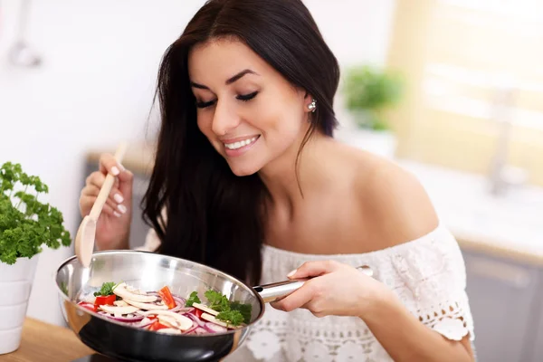 Jovem mulher preparando legumes fritos na cozinha — Fotografia de Stock