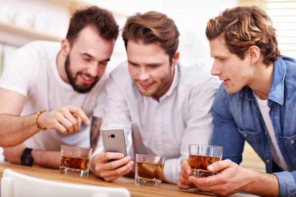 Glada vänner att ha kul med smartphone och dricka hemma — Stockfoto