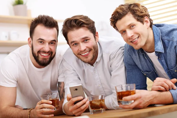 Amigos alegres que se divierten con el teléfono inteligente y beber en casa — Foto de Stock